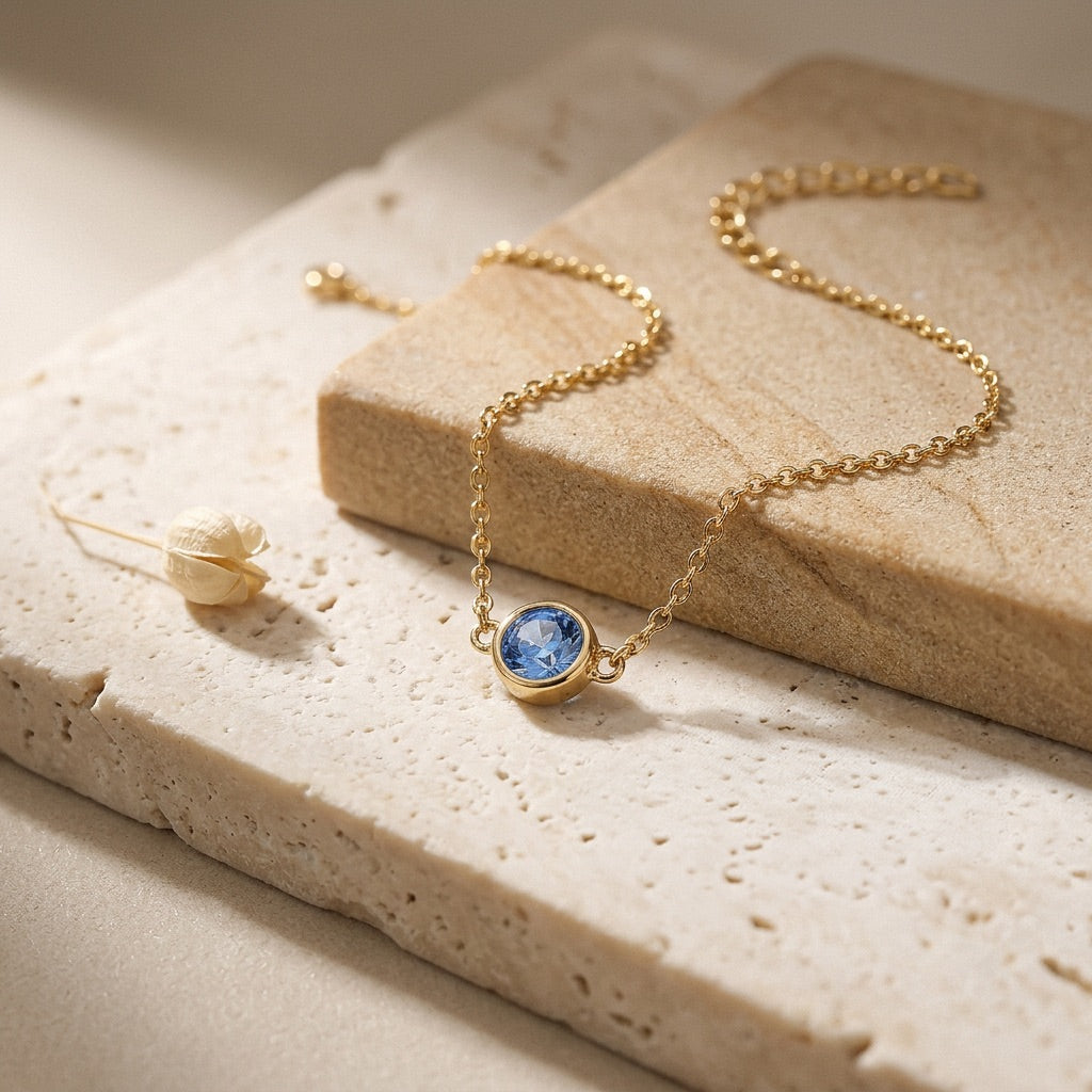 Gold necklace with a blue gemstone on a textured beige surface