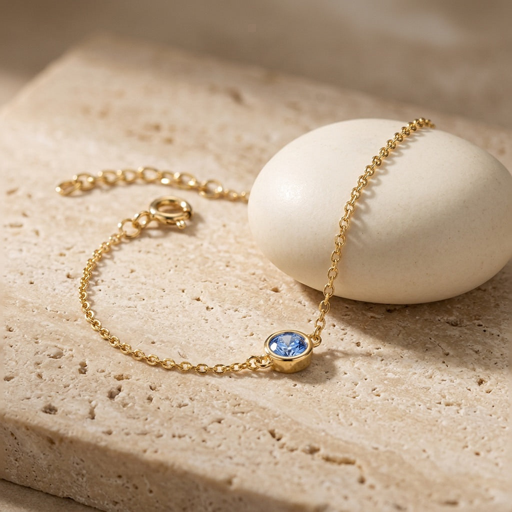 Gold bracelet with a blue gemstone on a beige stone surface