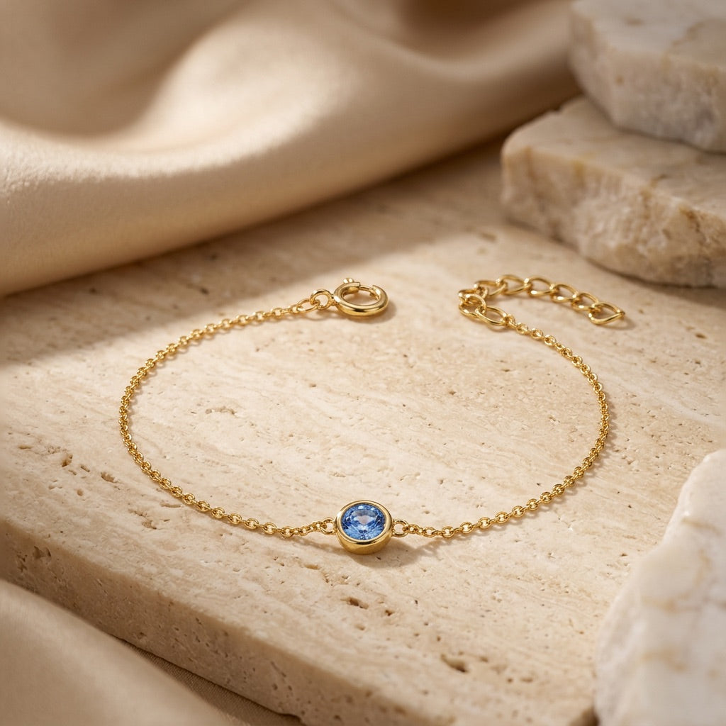 Gold bracelet with a blue gemstone on a beige stone surface