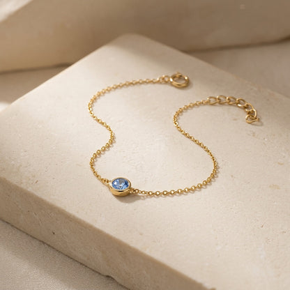 Gold bracelet with a blue gemstone on a beige surface
