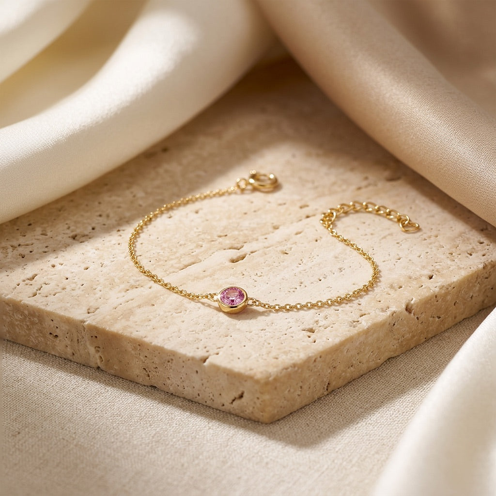 Gold bracelet with a pink gemstone on a beige stone surface