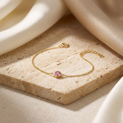 Gold bracelet with a pink gemstone on a beige stone surface