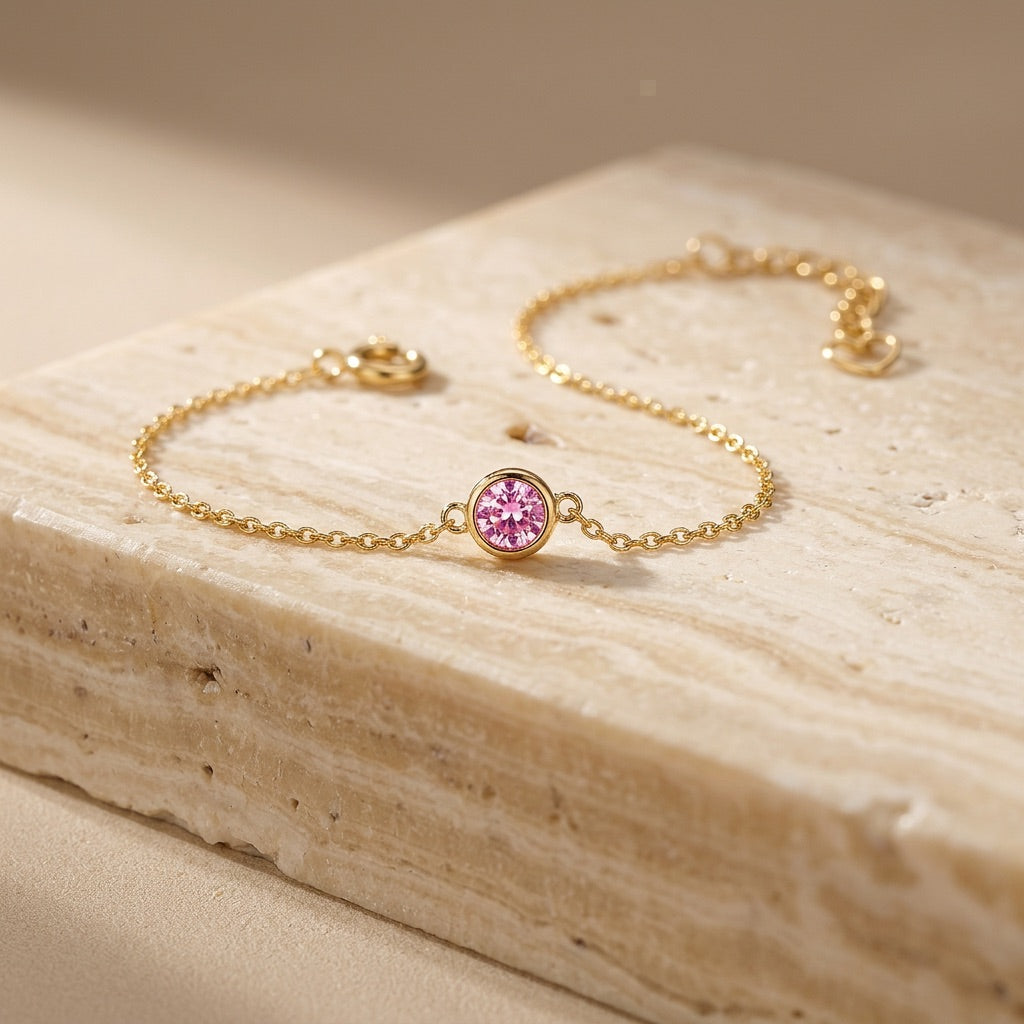 Gold bracelet with a pink gemstone on a beige stone surface