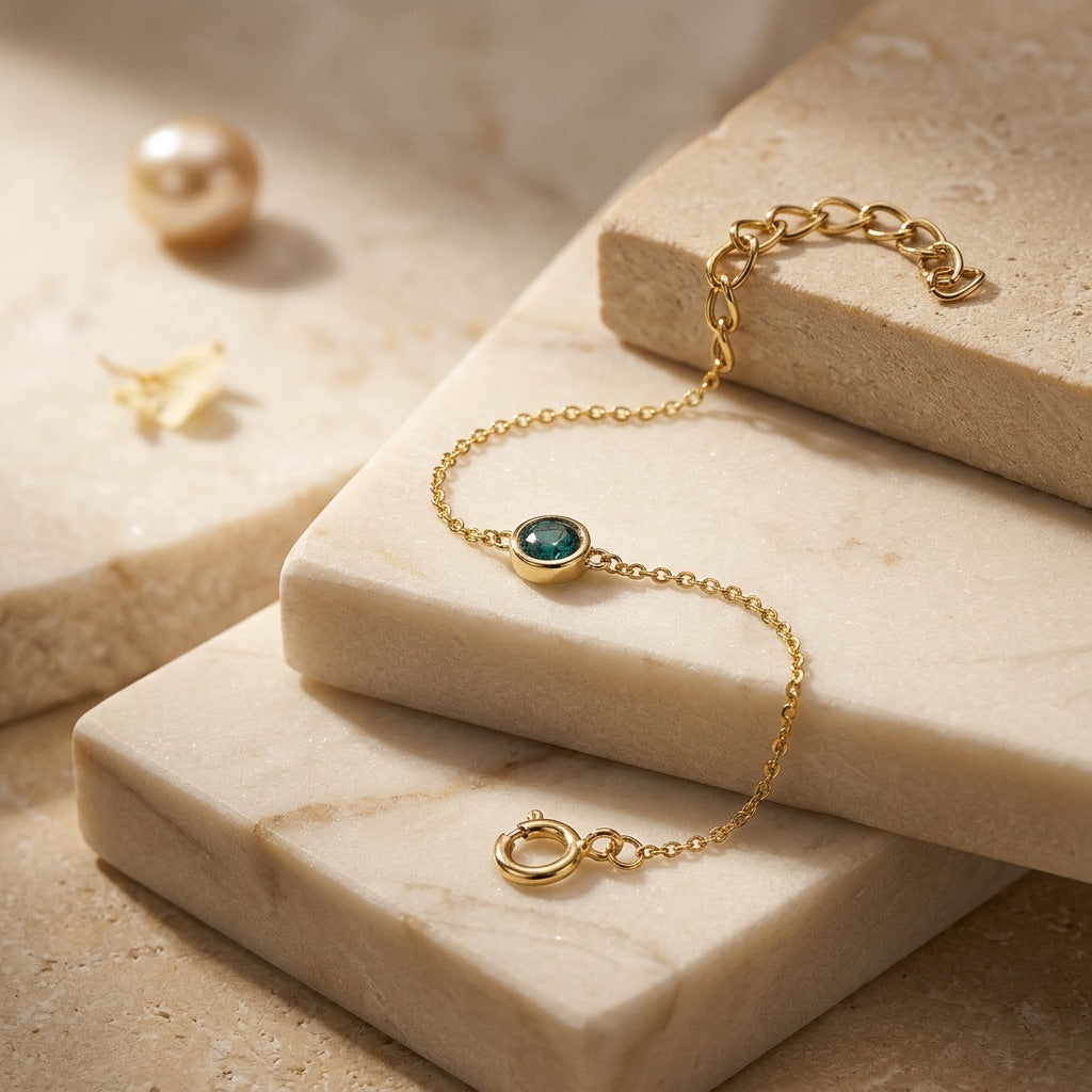 Gold bracelet with a green gemstone on a beige stone surface