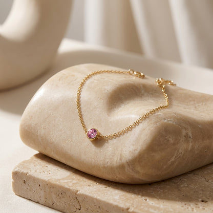 Gold bracelet with a pink gemstone on a beige stone surface