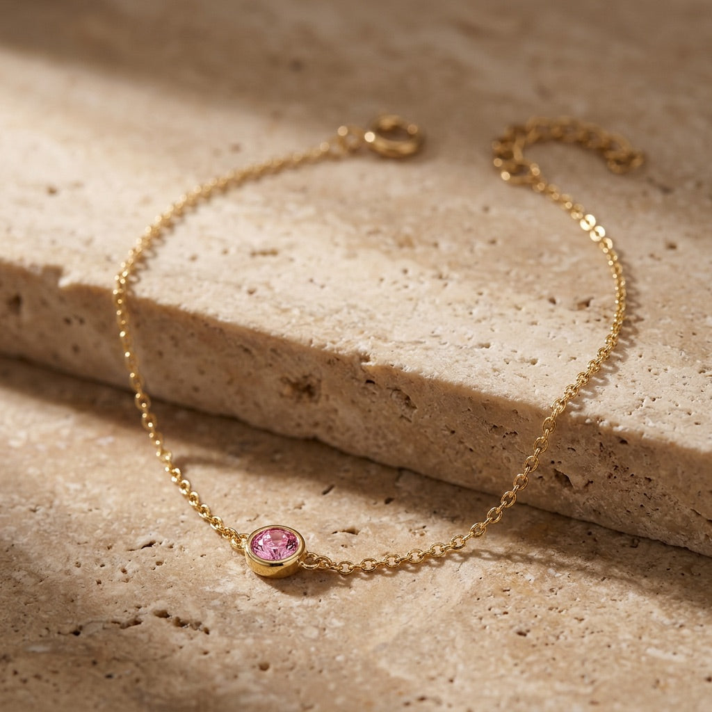 Gold bracelet with a pink gemstone on a beige stone surface