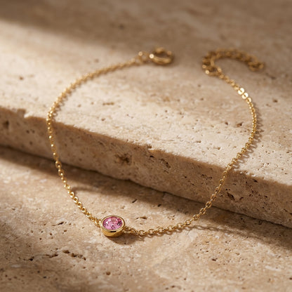 Gold bracelet with a pink gemstone on a beige stone surface