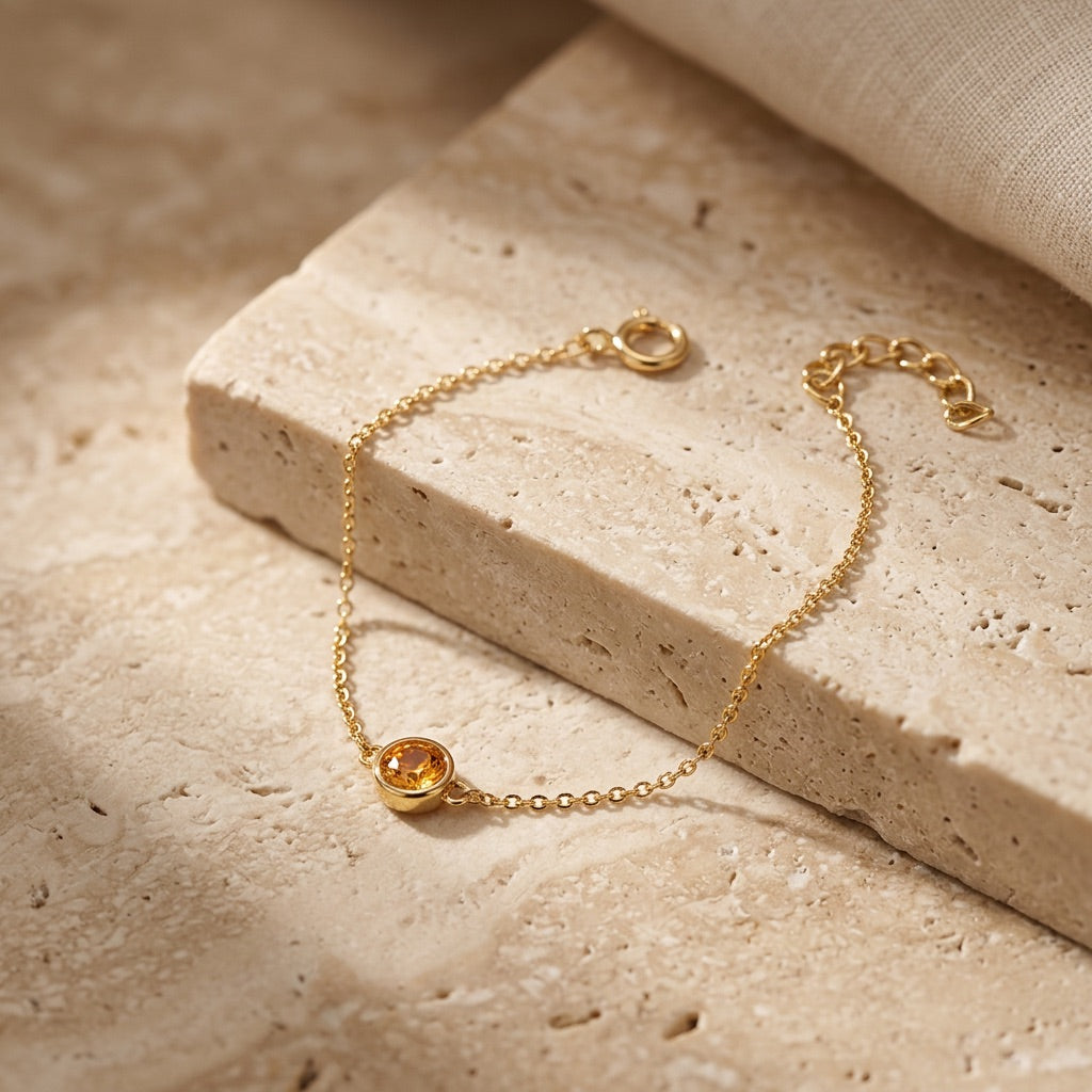 Gold bracelet with a yellow gemstone on a beige stone surface