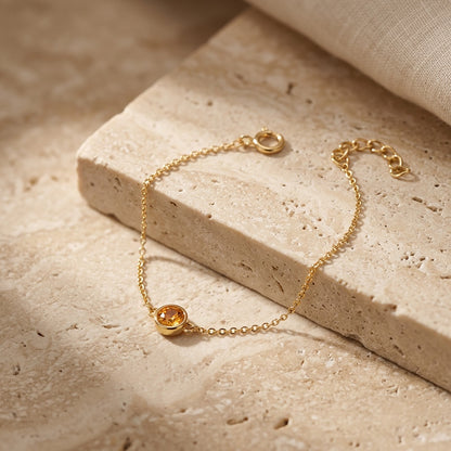 Gold bracelet with a yellow gemstone on a beige stone surface