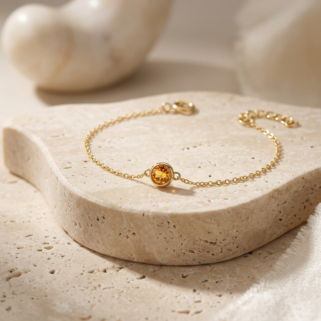 Gold bracelet with a yellow gemstone on a beige stone surface