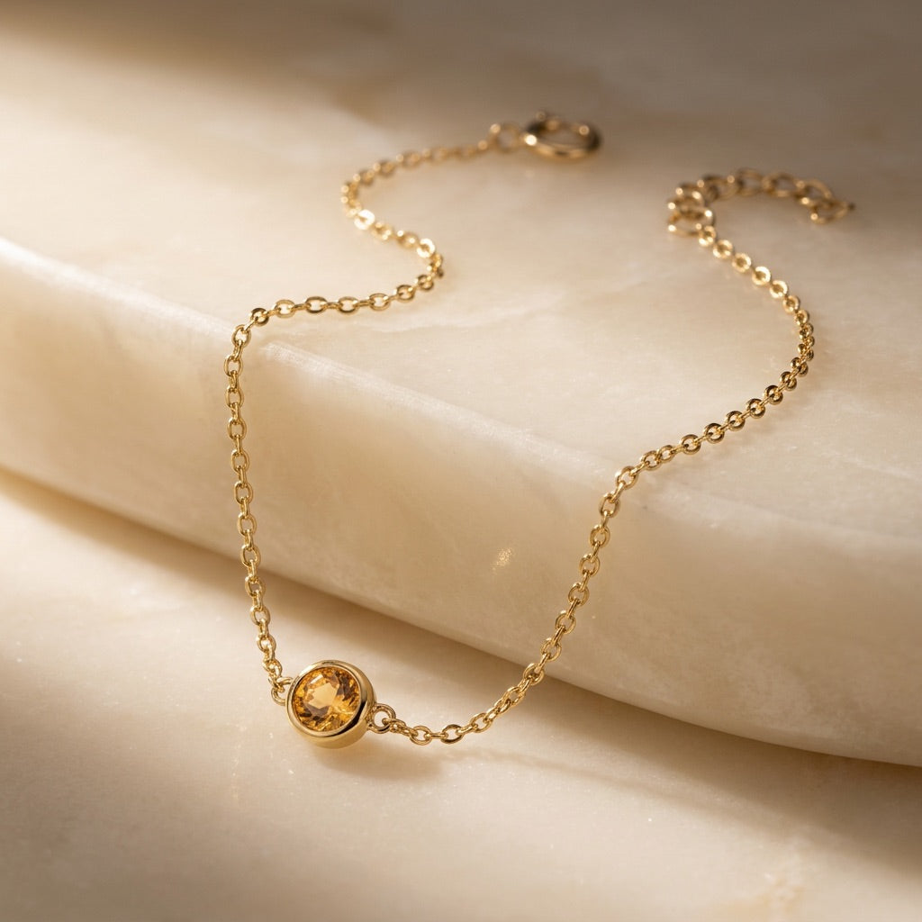 Gold bracelet with a yellow gemstone on a beige surface
