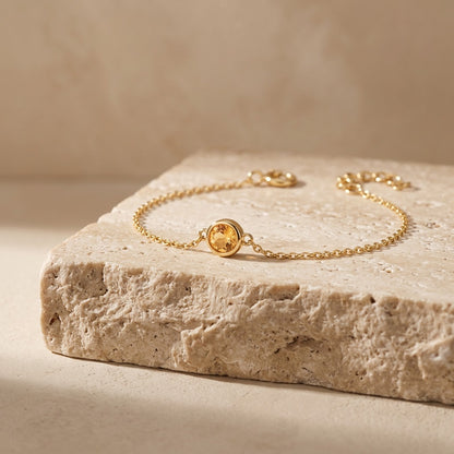 Gold bracelet with a yellow gemstone on a textured stone surface