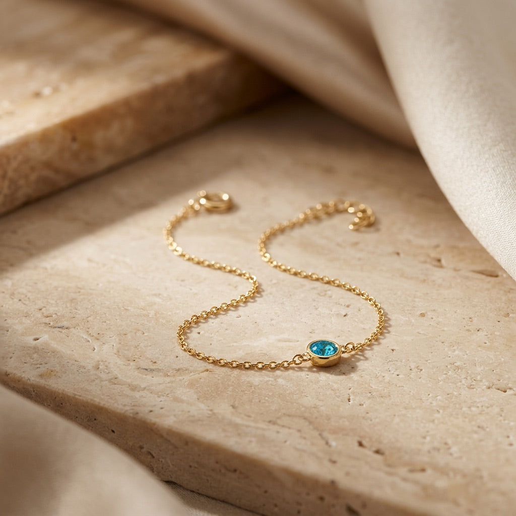 Gold bracelet with a blue gemstone on a beige stone surface