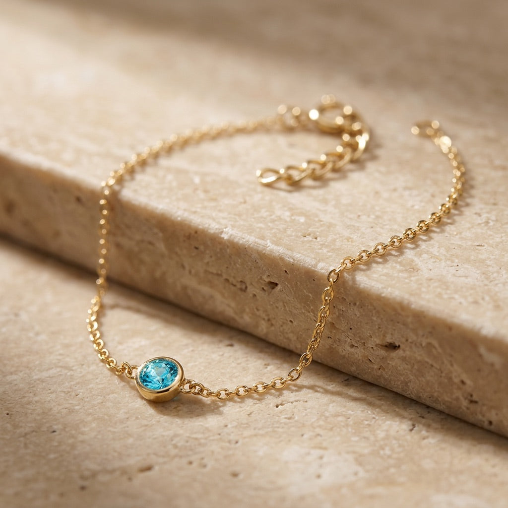 Gold bracelet with a blue gemstone on a beige stone surface