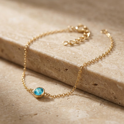 Gold bracelet with a blue gemstone on a beige stone surface