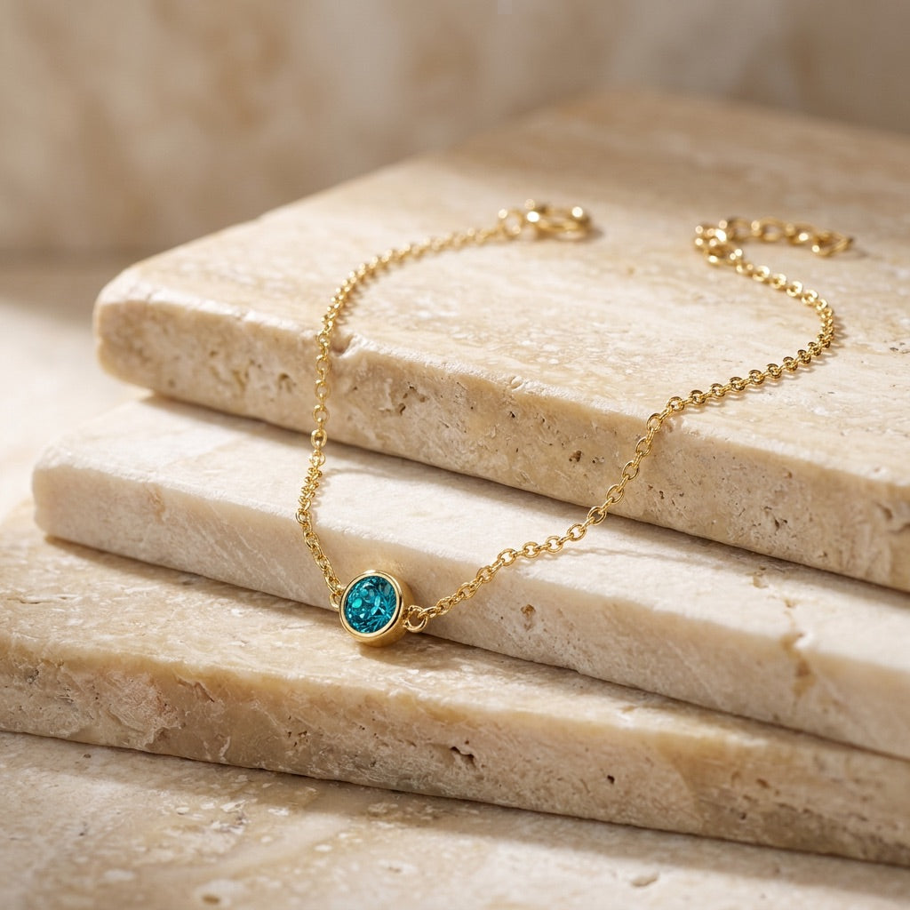 Gold bracelet with a blue gemstone on a stone surface