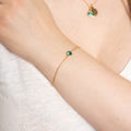 Gold ring with a green gemstone on a person's finger against a white background