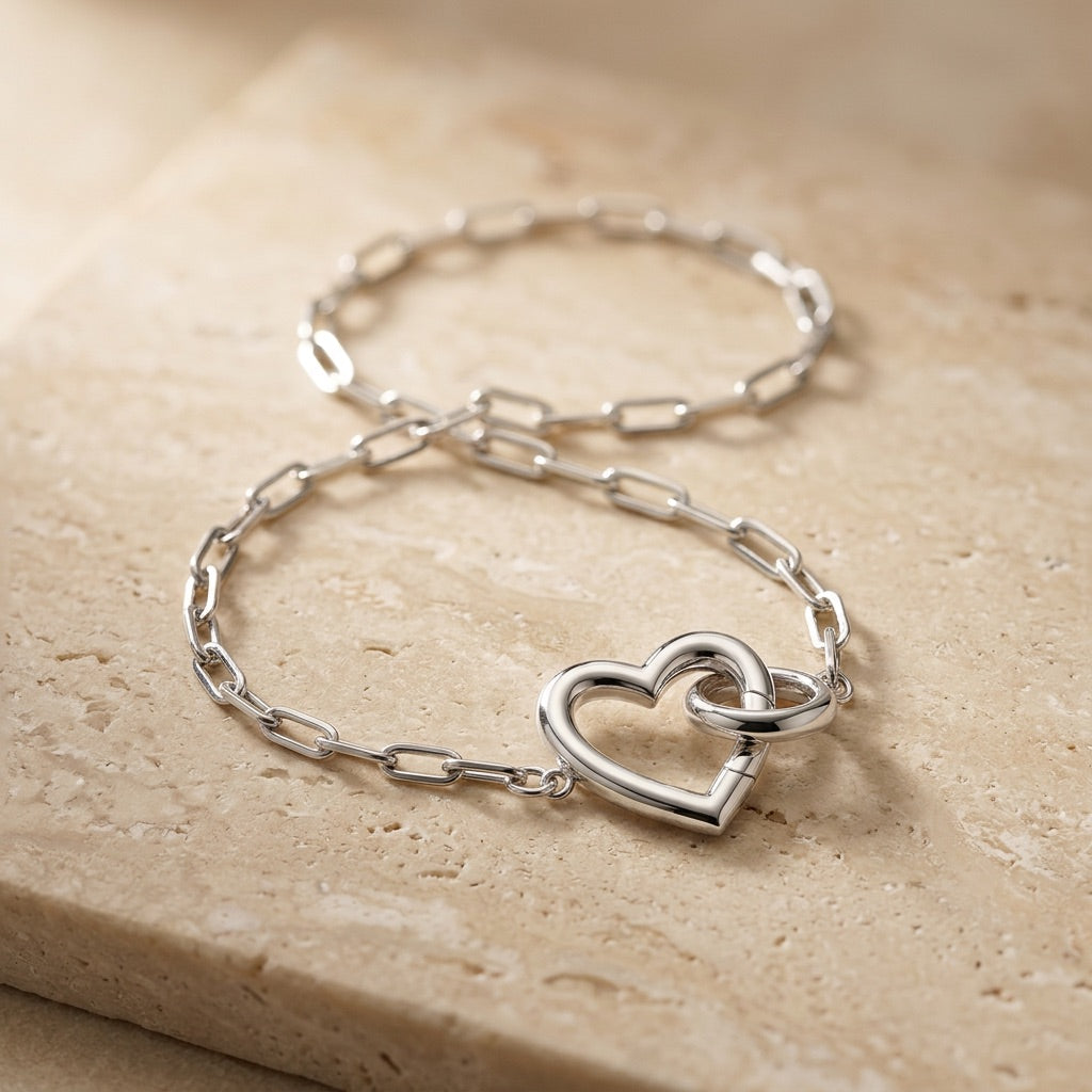 Silver bracelet with a heart-shaped clasp on a beige stone surface