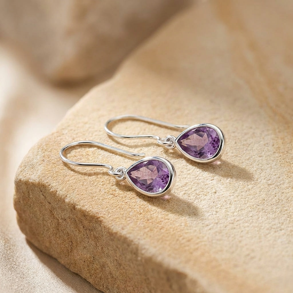Silver earrings with purple gemstones on a beige stone surface