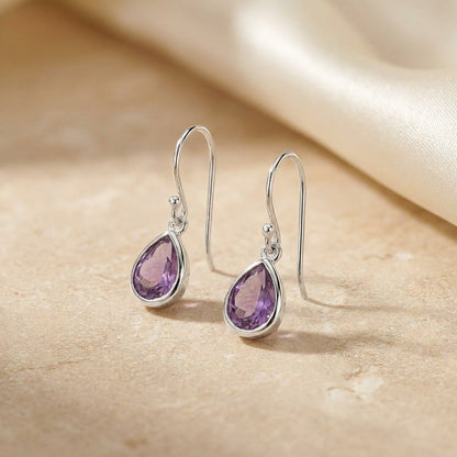 Silver earrings with purple gemstones on a beige fabric background