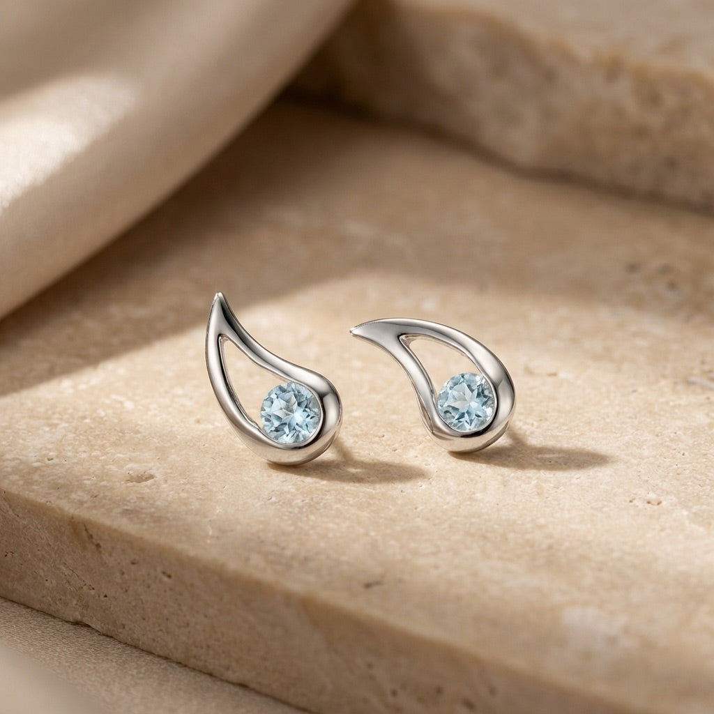 Silver earrings with blue gemstones on a beige stone surface