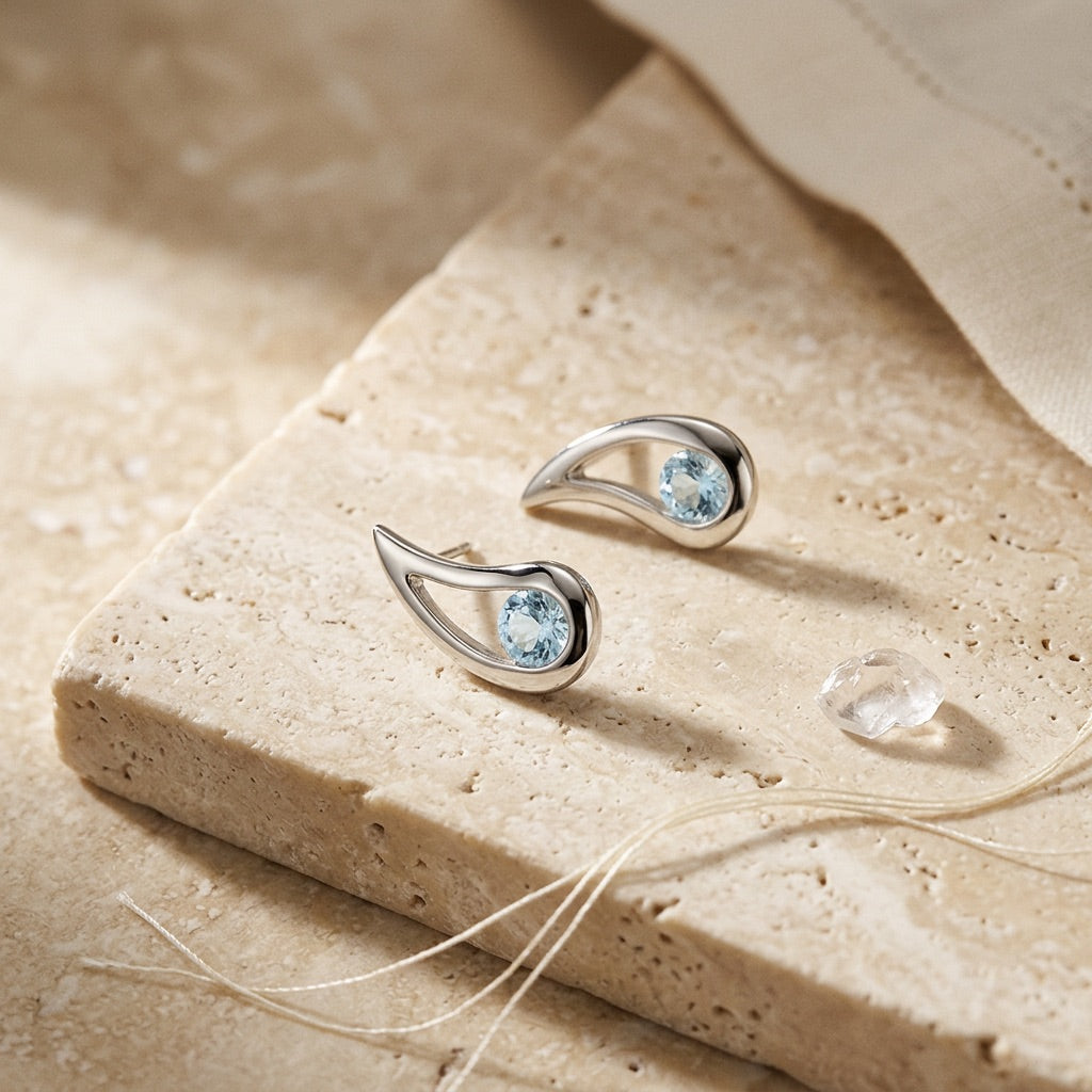 Silver earrings with blue gemstones on a beige stone surface