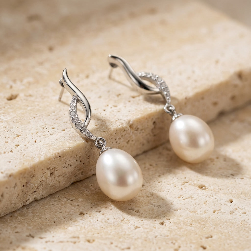 Pearl earrings with silver hooks on a beige stone surface