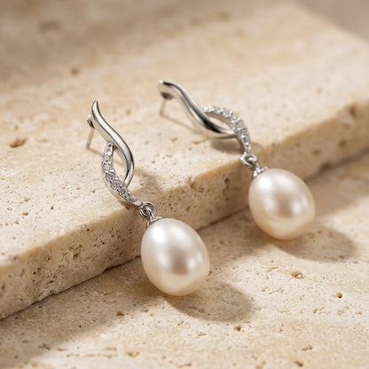 Pearl earrings with silver hooks on a beige stone surface
