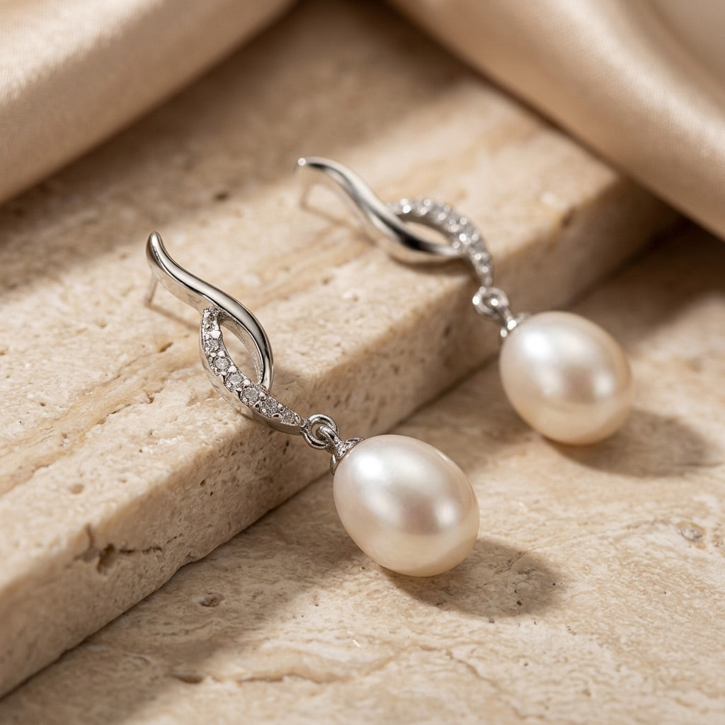 Pearl earrings with silver hooks on a beige stone surface