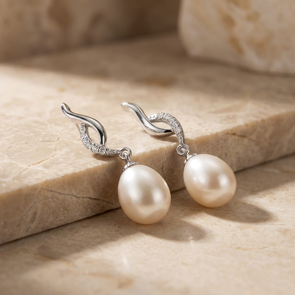 Pearl earrings with silver hooks on a beige stone surface