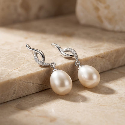 Pearl earrings with silver hooks on a beige stone surface
