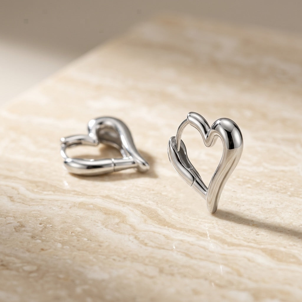 Heart-shaped silver earrings on a beige surface