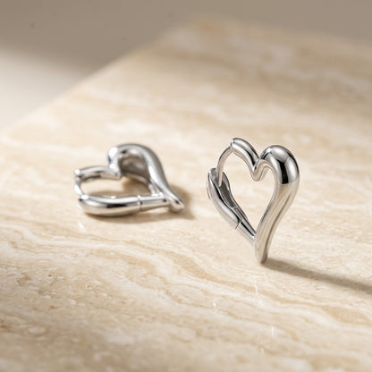 Heart-shaped silver earrings on a beige surface