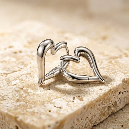 Silver cufflinks shaped like interlocking hearts on a textured stone surface