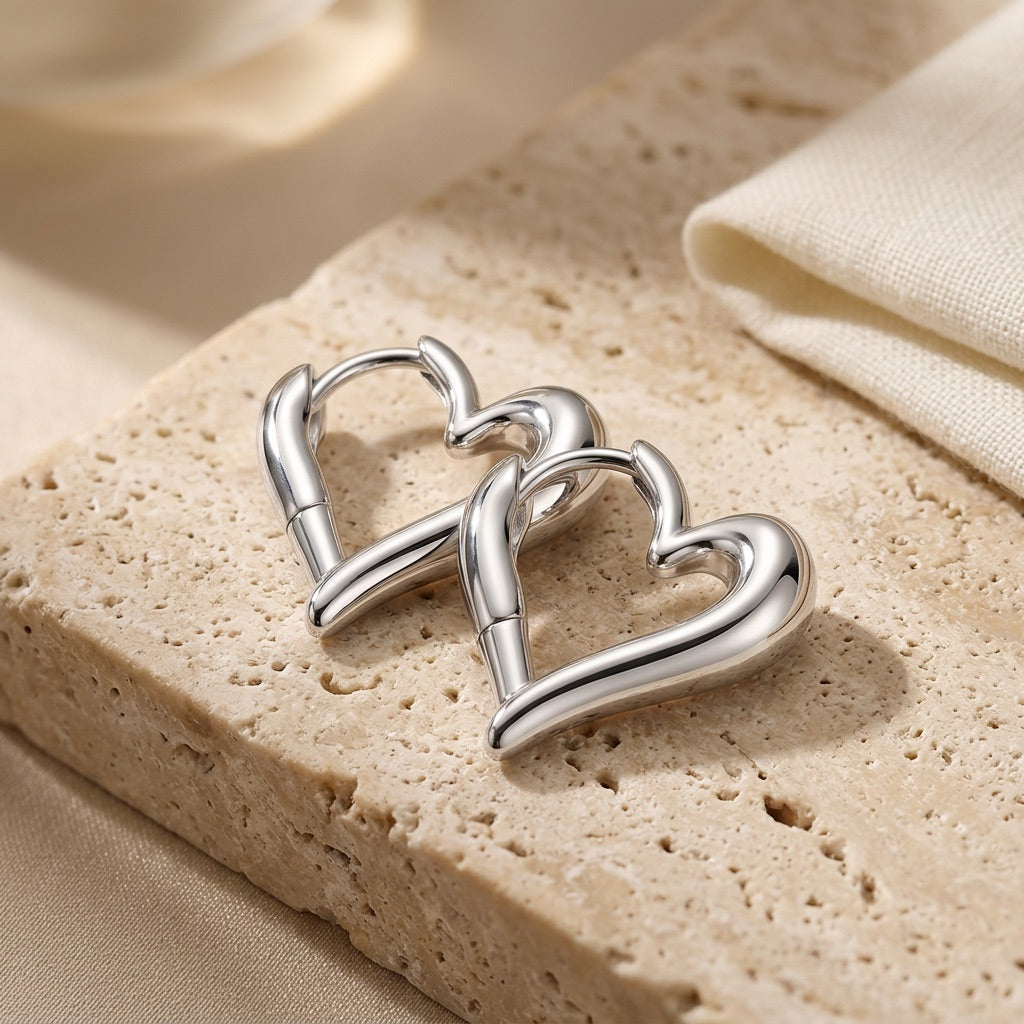 Silver heart-shaped earrings on a textured beige surface