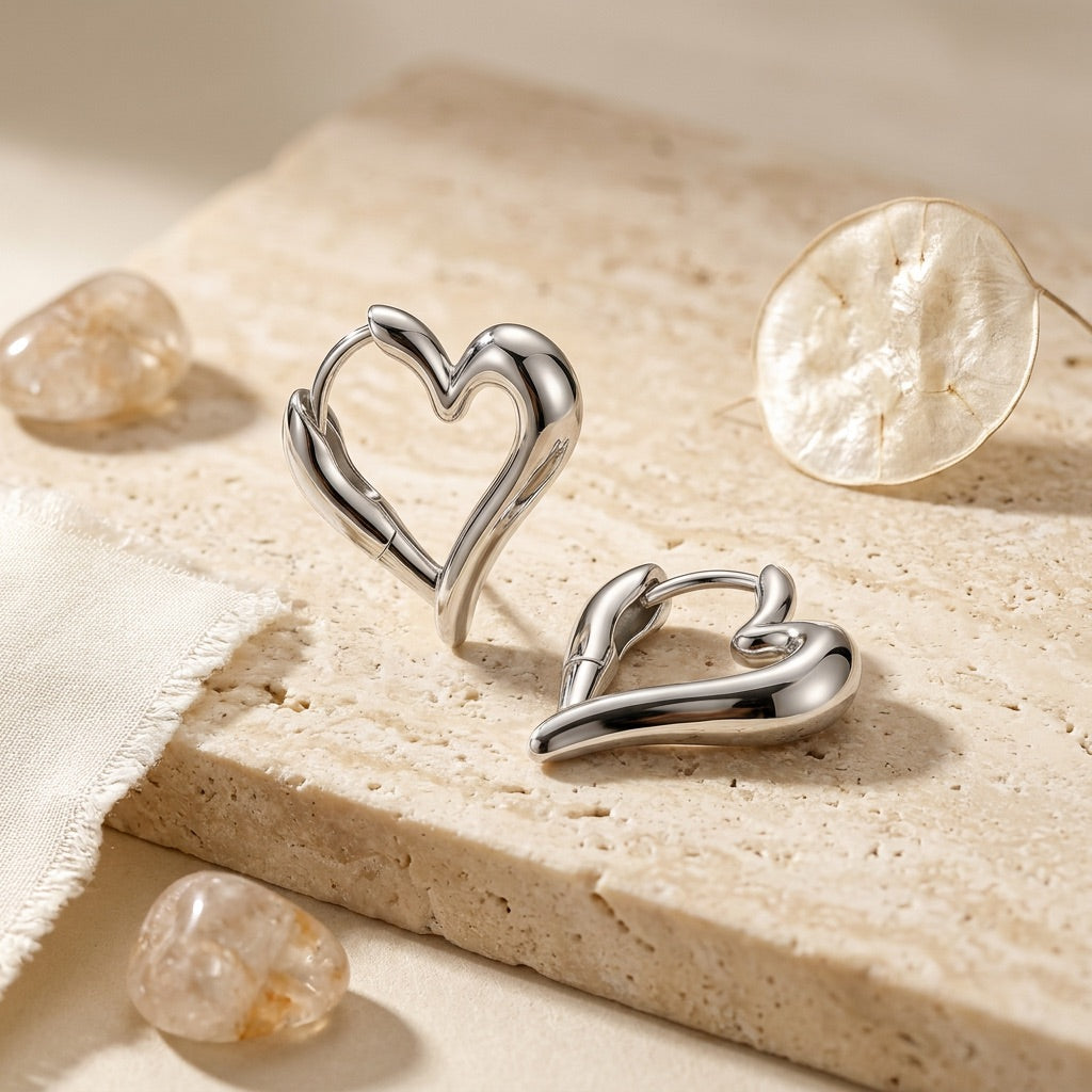 Silver heart-shaped earrings on a textured beige surface with crystals.