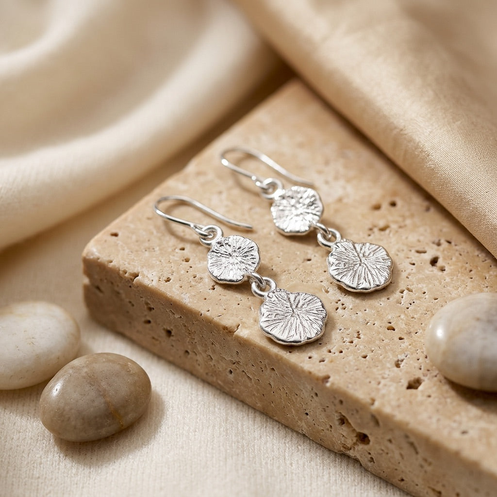 Silver earrings on a textured stone surface with stones around