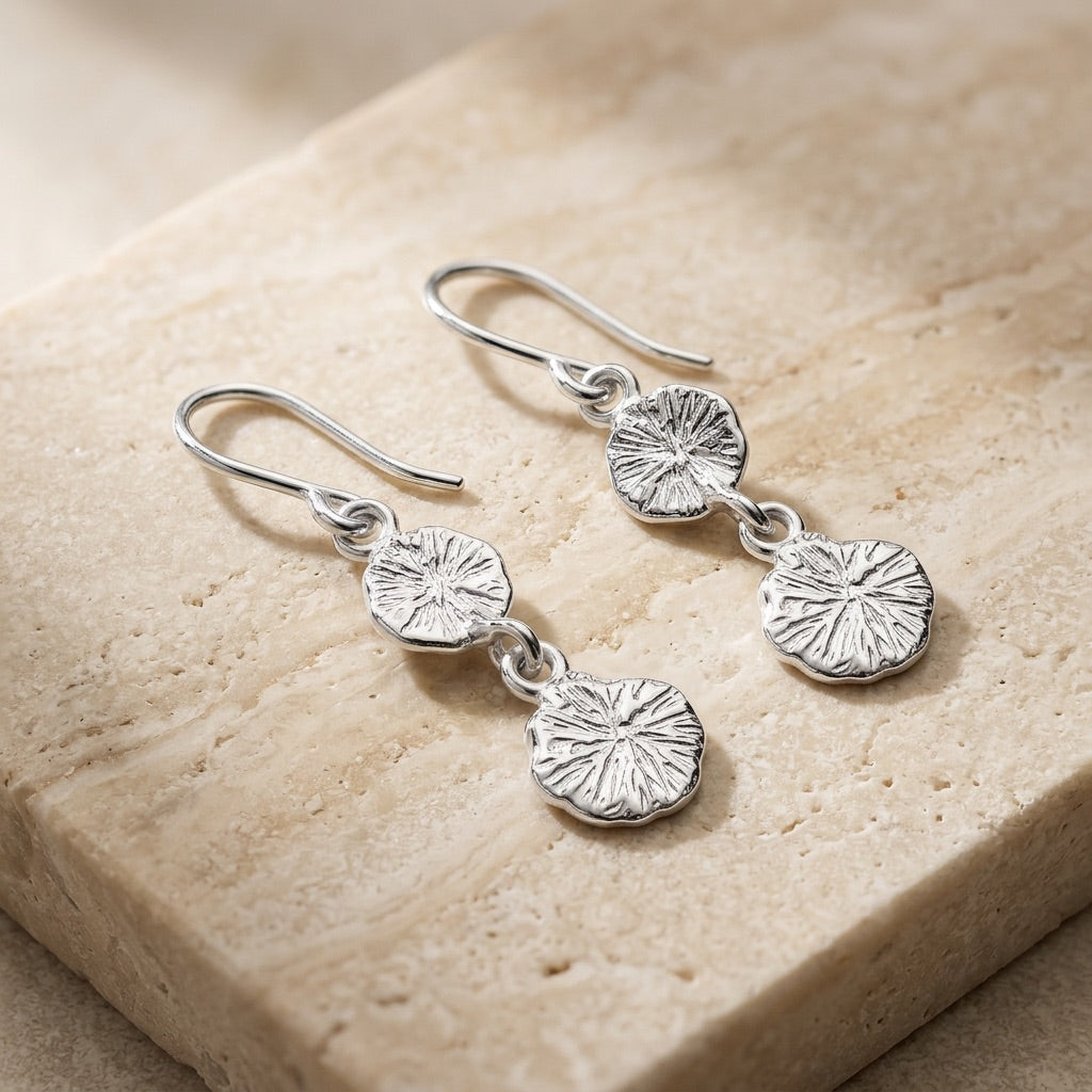 Silver earrings with circular designs on a beige stone surface