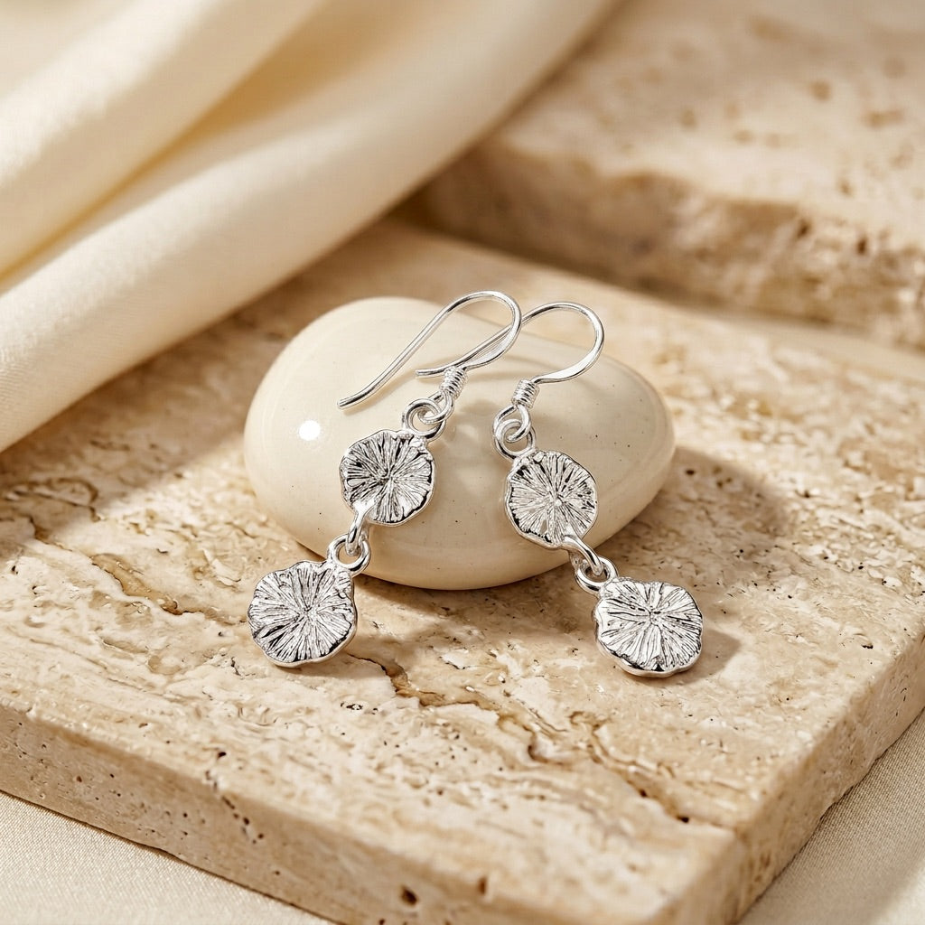 Silver earrings with floral designs on a stone surface