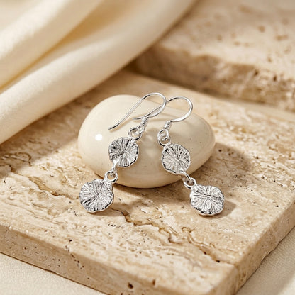 Silver earrings with floral designs on a stone surface