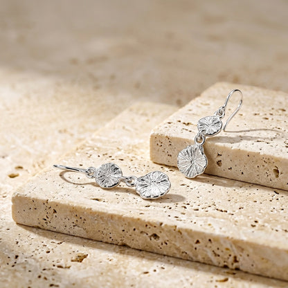 Silver earrings on a textured stone surface