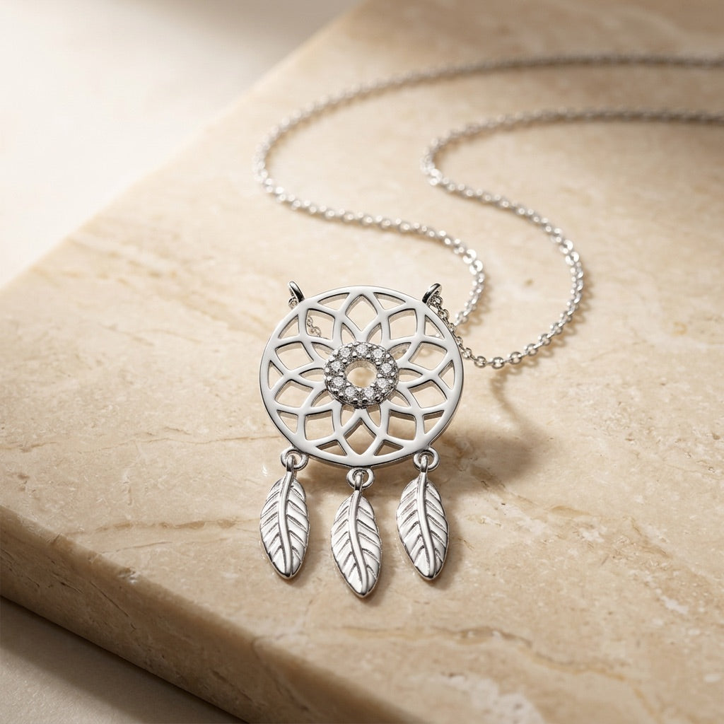 Silver dreamcatcher necklace on a beige stone surface