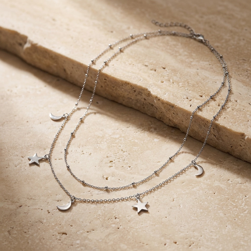 Silver necklace with star and moon charms on a beige stone surface