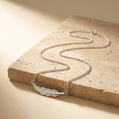 Silver necklace with a leaf pendant on a beige stone surface