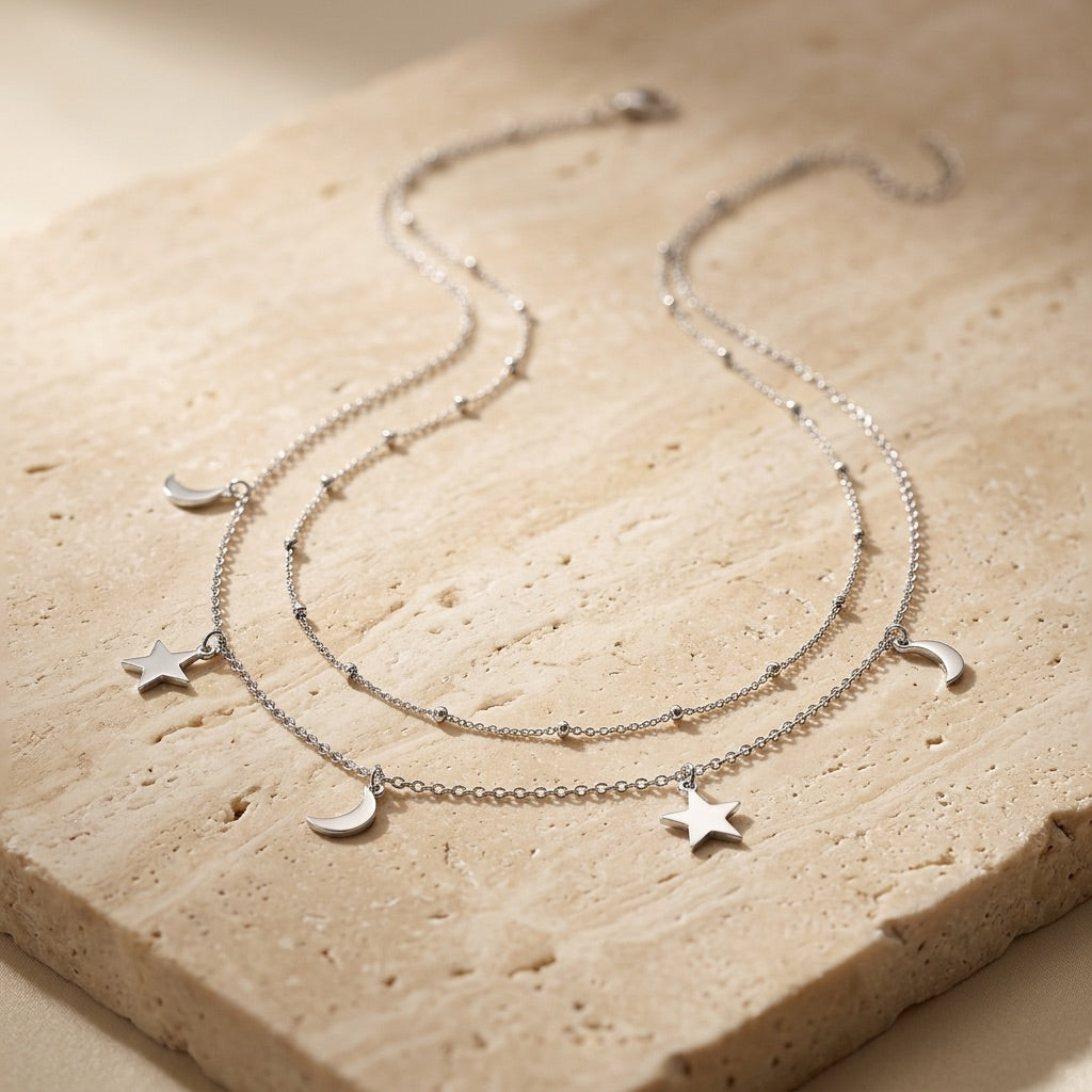 Silver necklace with star and moon charms on a beige stone surface