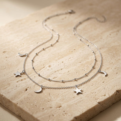 Silver necklace with star and moon charms on a beige stone surface
