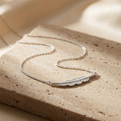 Silver feather necklace on a textured beige surface