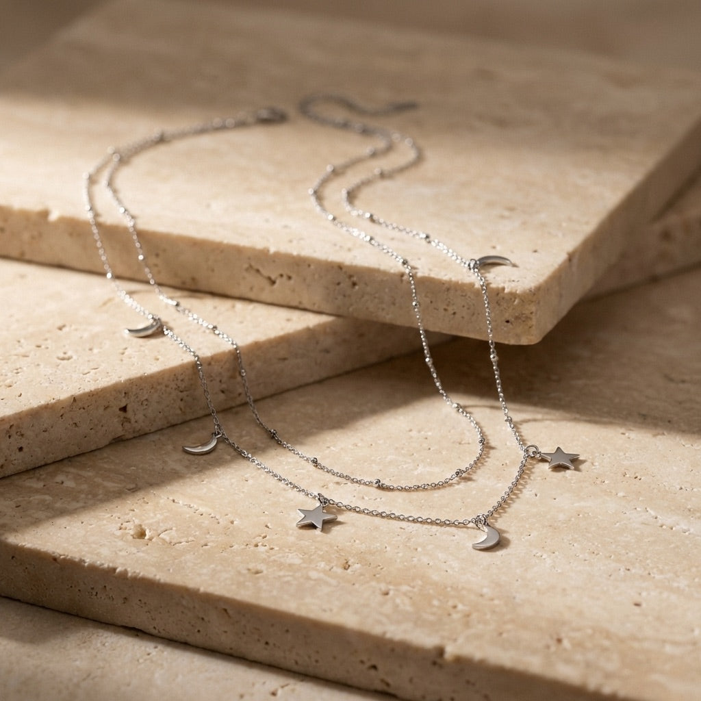 Silver necklace with star and moon charms on a beige stone surface
