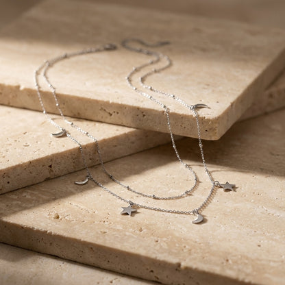 Silver necklace with star and moon charms on a beige stone surface