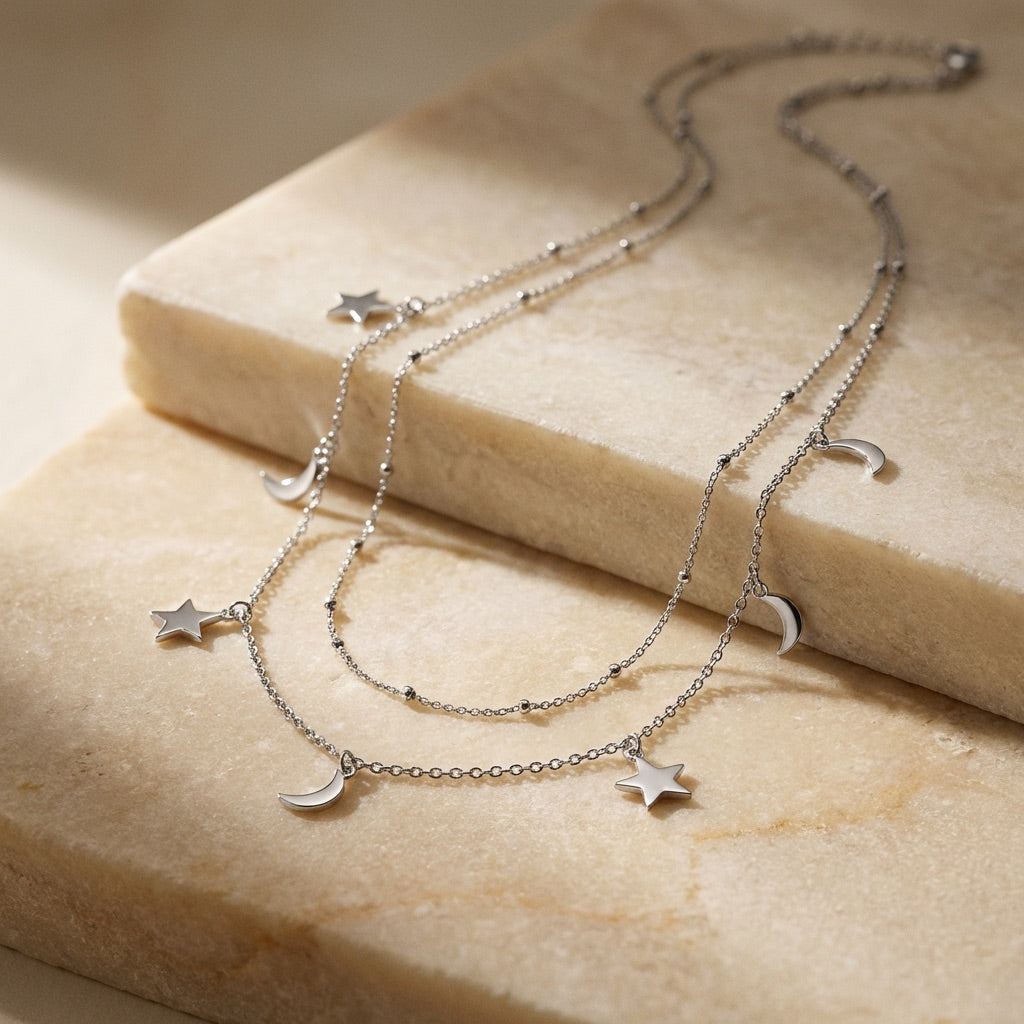 Silver necklace with star and moon charms on a beige stone surface